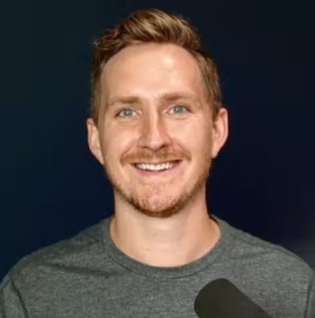 Headshot of Alban Brooke in front of a mic with a black background behind him