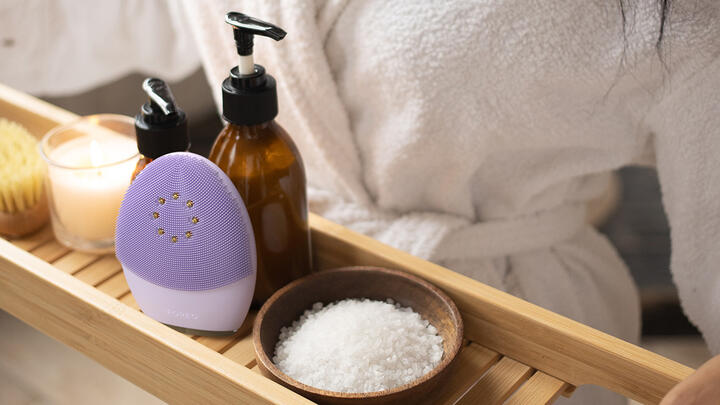 Hands holding a wooden tray with bath salt, liquid soap, and FOREO LUNA 4