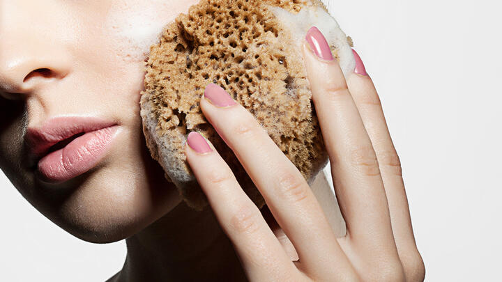 A caucasian woman face closeup, holding a natural sponge with large pores and washing her face