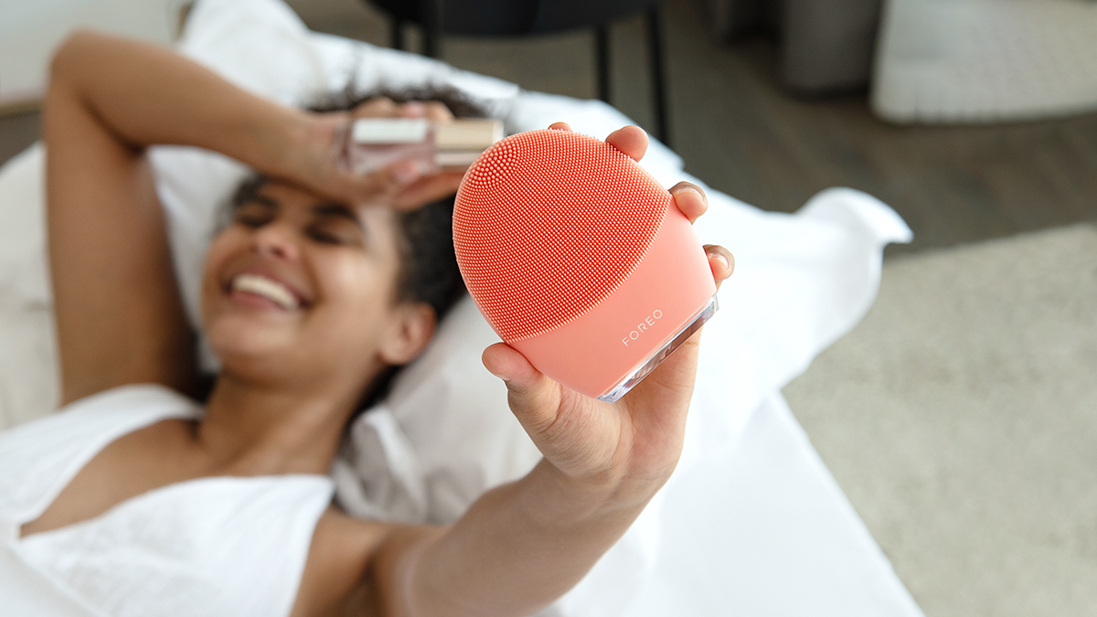 Smiling woman laying in bed, holding FOREO LUNA 4