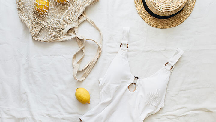 White swimsuit, straw hat, and a natural bag with lemons on a white sheet